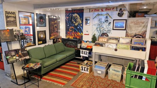 En soffhörna med musikrelaterade affischer på väggarna, hyllor och backar med LP-skivor.