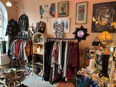 Delar av en butikslokal fylld av second hand-prylar, kläder, tavlor och speglar.